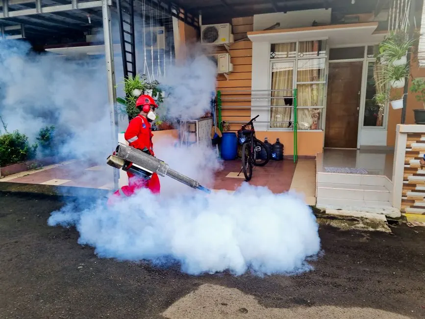 Pest control specialist using a smoke machine to fumigate outside a house.